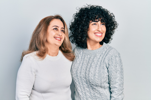 Madre e hija de Oriente Medio vistiendo ropa casual mirando hacia otro lado con sonrisa en la cara, expresión natural. riendo confiado.  - Foto, imagen