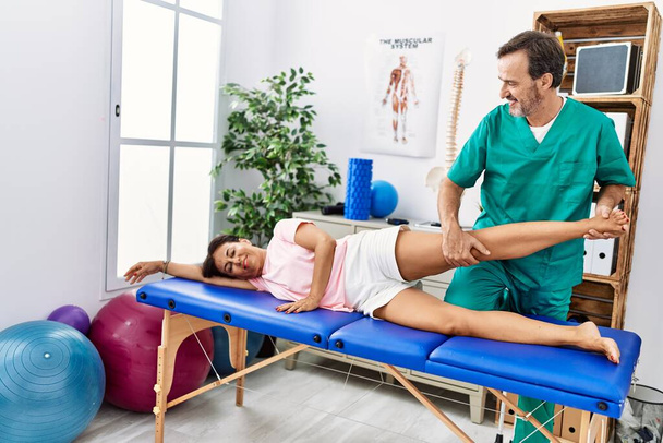 Чоловік і жінка середнього віку посміхаються впевнено розтягуючи ногу, що має сеанс реабілітації в клініці фізіотерапії
 - Фото, зображення
