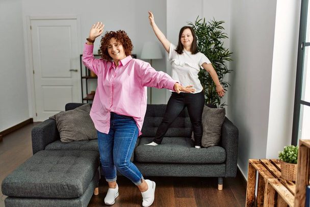 Mature mother and down syndrome daughter at home dancing on the sofa - Photo, image