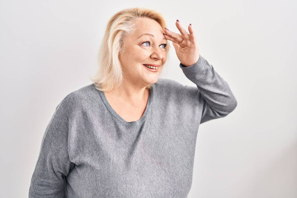 Middle age caucasian woman standing over white background very happy and smiling looking far away with hand over head. searching concept.  - Valokuva, kuva