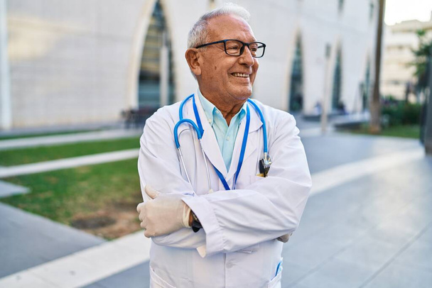 Senior man wearing doctor uniform standing with arms crossed gesture at street - Photo, Image