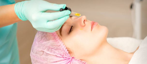 Young white woman getting acid organic retinol peel face skin with the pipette in a beauty clinic - Photo, Image