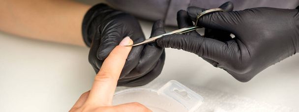 Mestre de manicure remove cutículas de unhas femininas com tesoura usando luvas de proteção no salão de manicure - Foto, Imagem