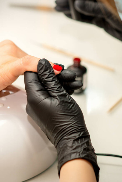 Manicure varnish painting. Close-up of a manicure master wearing rubber black gloves applying red varnish on a female fingernail in the beauty salon - Fotoğraf, Görsel