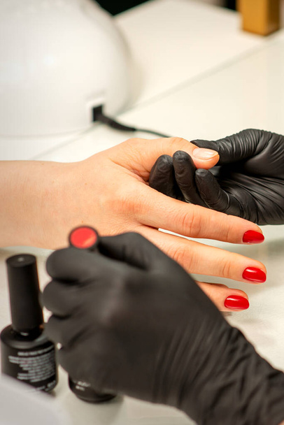 Professional manicure. A manicurist is painting the female nails of a client with red nail polish in a beauty salon, close up. Beauty industry concept - Zdjęcie, obraz