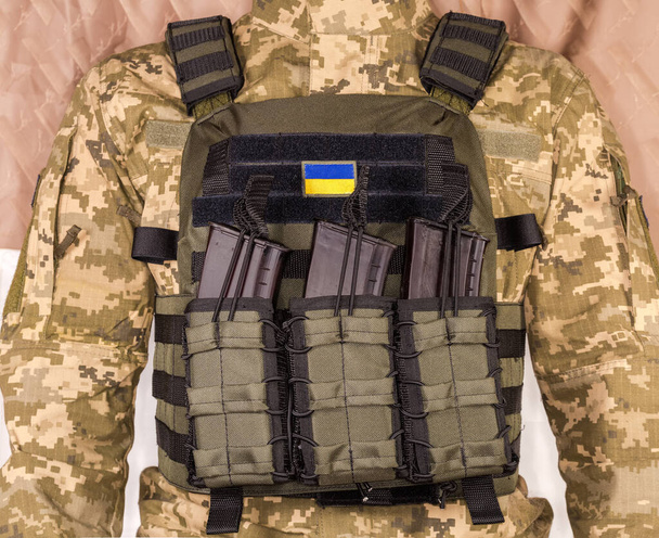 Military bulletproof vest with strapped in tactical pouches of cartridge rifle magazines wear by an Ukrainian soldier, view from the chest side - Photo, Image