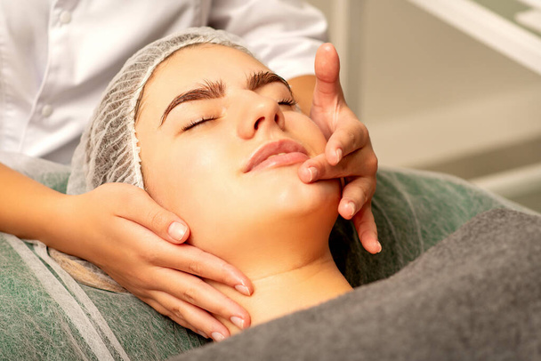 Massage du visage. Belle caucasienne jeune femme blanche ayant un massage facial avec les yeux fermés dans un salon de spa - Photo, image