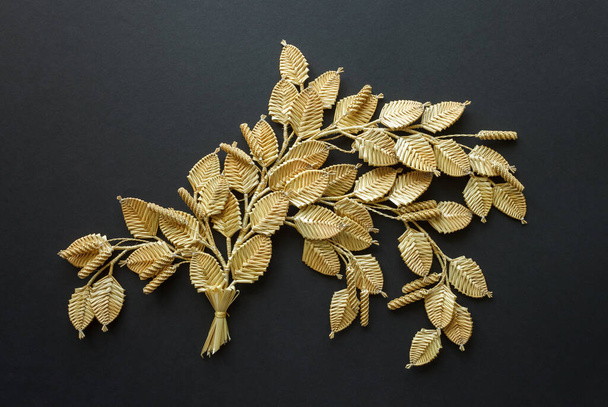 The branch with leaves is made of straw. Straw wall decoration. The products are made of straw. Decoration of straw on a dark background. - Valokuva, kuva