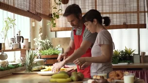 onnellista kypsä pari keittiössä modernin huoneiston, valmistelee hedelmiä jälkiruoka samalla hauskaa - Materiaali, video