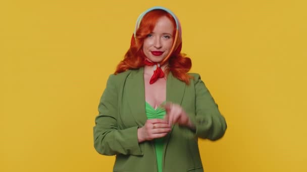 Piros hajú fiatal nő zöld kabátban győzelmi jelet mutat, remélve a sikert és a győzelmet, békemozgást végez, kedves optimista arckifejezéssel mosolyog. Ginger lány beltéri elszigetelt sárga háttér - Felvétel, videó
