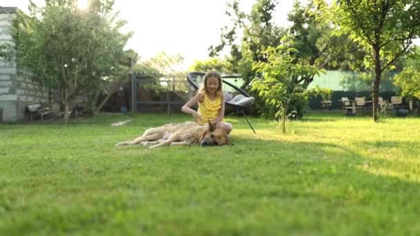 Linda chica y perro viejo disfrutar del día de verano en la hierba en el parque. Niños y animales en el patio trasero de casa, felices. Amor mascotas. - Metraje, vídeo