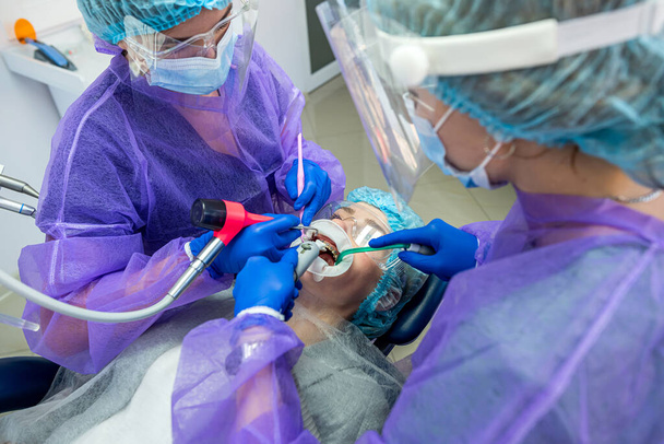 два красивых помощника в специальной одежде маски шляпы перчатки помогают провести операцию к стоматологу. Понятие стоматологической хирургии - Фото, изображение