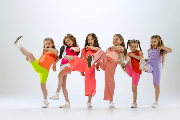 Modern koreografi dersi. Beyaz stüdyo arka planında izole halde dans eden parlak renkli elbiseli, mutlu ve aktif küçük kızlardan oluşan bir dans grubu. Müzik, moda, sanat, çocukluk, hobi kavramı. - Fotoğraf, Görsel