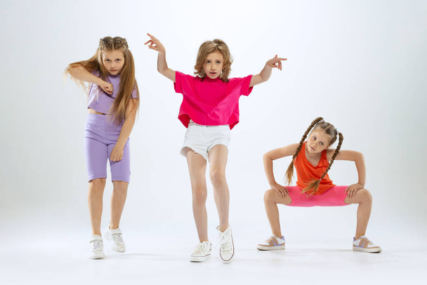 Joy, fun and happiness. Portrait of happy, active little girls, happy kids in bright colorful clothes dancing isolated on white studio background. Concept of music, fashion, art, childhood, hobby. - Фото, изображение