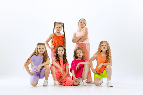 Modern choreography lesson. Dance group of happy, active little girls in bright colorful clothes dancing isolated on white studio background. Concept of music, fashion, art, childhood, hobby. - Foto, afbeelding