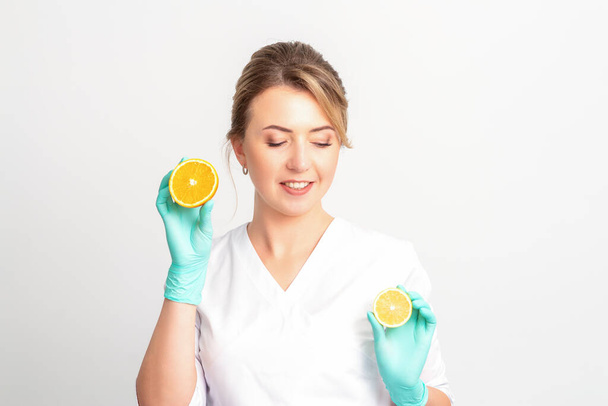 Nutricionista femenina sonriente sosteniendo una naranja en rodajas, mirando a la cámara sobre fondo blanco, concepto de dieta saludable - Foto, Imagen