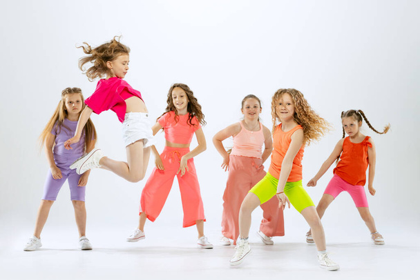 Joy, fun and happiness. Portrait of happy, active little girls, happy kids in bright colorful clothes dancing isolated on white studio background. Concept of music, fashion, art, childhood, hobby. - Fotoğraf, Görsel