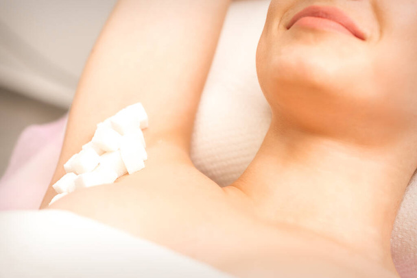 Sugaring, waxing concept. White sugar cubes lie down on the female armpit of the young white woman, close up - Photo, Image