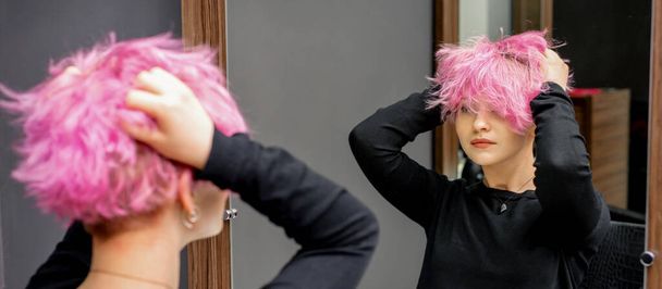 Genç kadın yeni kısa pembe saç stilini kontrol ediyor. Kuaförde elleri aynanın önünde.. - Fotoğraf, Görsel