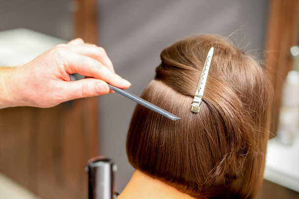 Перукар випрямляє коротке волосся молодої брюнетки з плоским залізом в перукарні, крупним планом
 - Фото, зображення