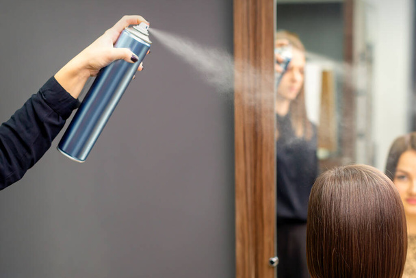 Перукар використовує спрей для волосся, щоб виправити коротку зачіску молодої брюнетки, сидячи в перукарні
 - Фото, зображення
