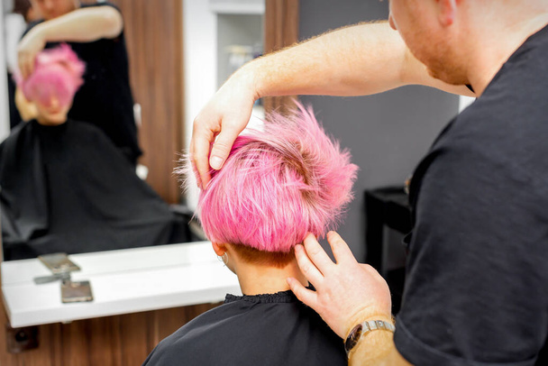 Fryzjer z rękami jest wymeldowanie i ustalenie krótkie różowe fryzury młodej białej kobiety w salonie fryzjerskim - Zdjęcie, obraz