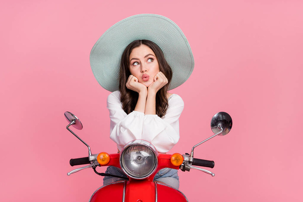 Photo of pretty minded person sit bike hands cheeks look interested empty space isolated on pink color background. - Zdjęcie, obraz