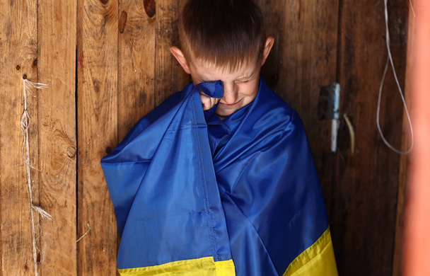 Rosja wojenna przeciwko Ukrainie. płaczący ukraiński chłopiec z flagą Ukrainy na zewnątrz. Przerwać wojnę. antywojenny protest, płacz depresja rozpacz, nadzieja na pokój ludzki, stres przerażenie ocieplający strach. - Zdjęcie, obraz