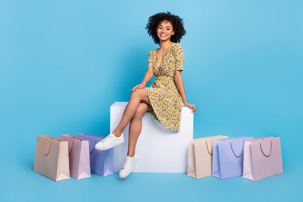 Photo of charming dreamy lady dressed print outfit sitting cube chair shopping bags isolated blue color background. - Fotoğraf, Görsel