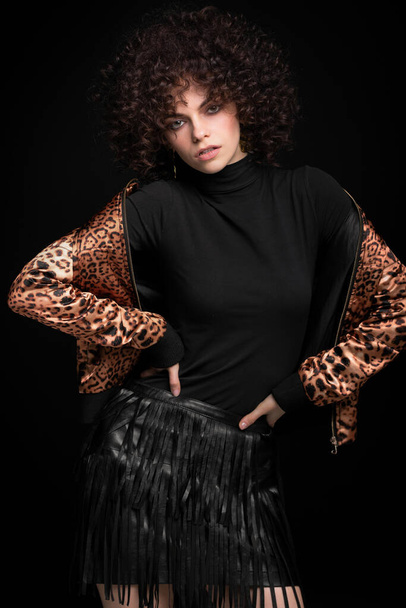 Fashionable portrait of a white Caucasian girl with African curls. Girl in a leopard-print jacket on a black background - Fotografie, Obrázek