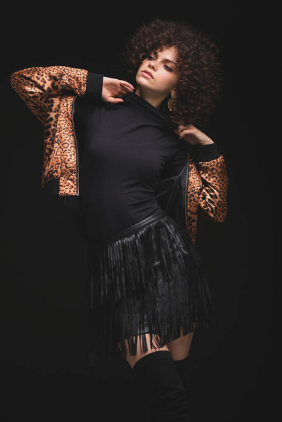 Fashionable portrait of a white Caucasian girl with African curls. Girl in a leopard-print jacket on a black background - Photo, Image