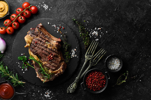 cowboy steak with spices on a stone background, first-class rib on the bone, top view. On a black stone background. - Foto, immagini