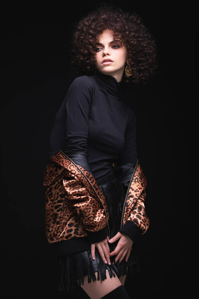 Fashionable portrait of a white Caucasian girl with African curls. Girl in a leopard-print jacket on a black background - Photo, Image