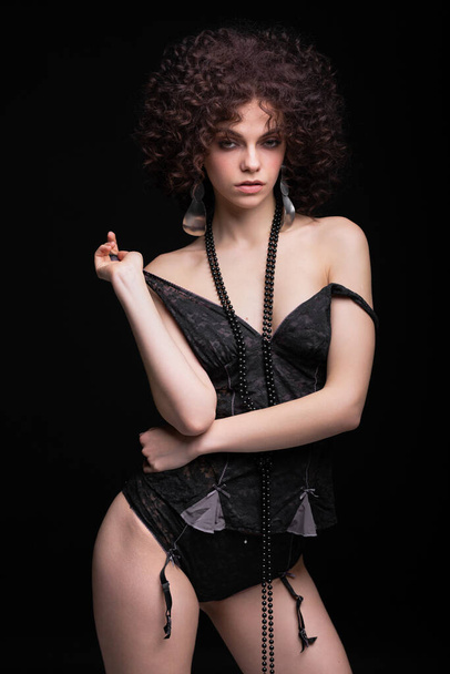 Sexy slender girl in black lingerie on a black background. Model with African curls. Afro hairstyle - Photo, Image