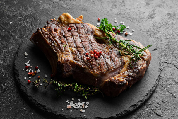 Juicy grilled steak on the bone cooked on the grill. Barbecue. On a black stone background. - Фото, зображення