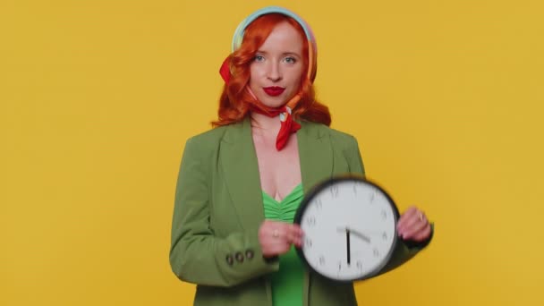 É a tua vez. Ruiva jovem mulher em casaco verde e vestido mostrando o tempo na parede do relógio do escritório, ok, polegar para cima, aprovar, apontando o dedo para a câmera. Menina de gengibre dentro de casa isolado no fundo amarelo - Filmagem, Vídeo