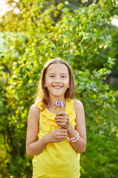 Chica feliz con frenillos comiendo helado italiano cono sonriendo mientras descansa en el parque en el día de verano, niño disfrutando de helado al aire libre, felices fiestas, verano - Foto, Imagen
