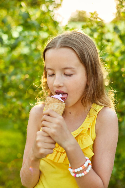 Szczęśliwa dziewczyna z aparatem na zęby jedząca włoskie lody uśmiechnięta podczas odpoczynku w parku w letni dzień, dziecko cieszące się lodami na świeżym powietrzu, szczęśliwe wakacje, lato - Zdjęcie, obraz