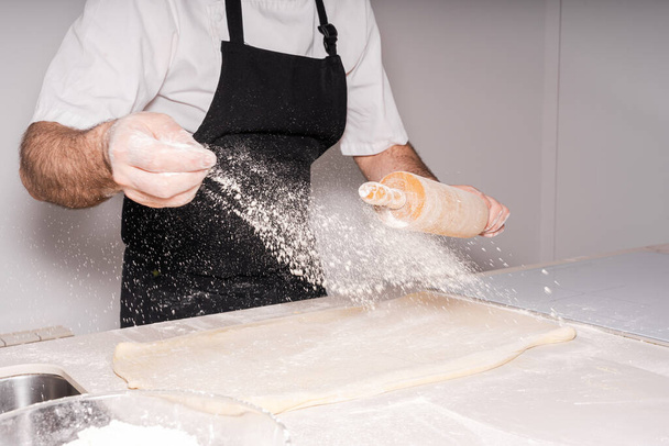 Man cooking homemade croissants, preparing the puff pastry and adding flour - Foto, afbeelding