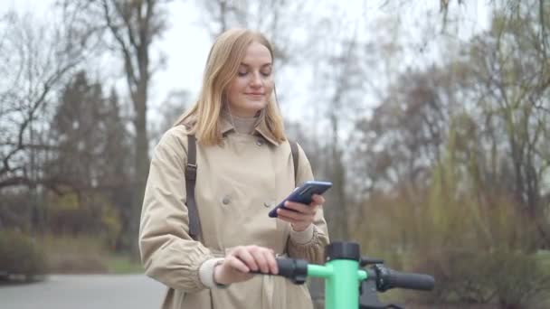 Γυναίκα λάβει ηλεκτρικά σκούτερ Kick ή ποδήλατο στο μοίρασμα πάρκινγκ, τουριστική εφαρμογή τηλεφώνου στο δρόμο. Οικολογική μεταφορά στην πόλη - Πλάνα, βίντεο