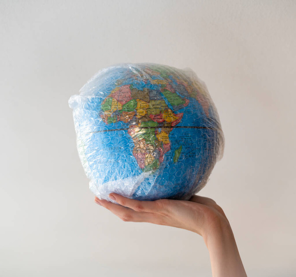 Main tient un globe enveloppé dans un emballage à bulles en plastique. - Photo, image