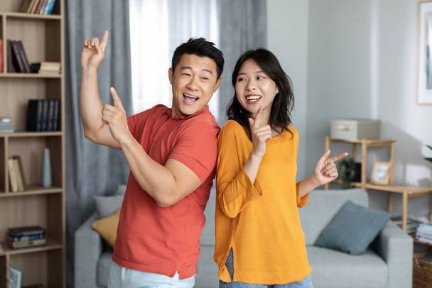 Funny asian man and woman in casual outfits having good time together at home, happy chinese husband and wife enjoying weekend, singing songs and dancing, copy space. Domestic lifestyle concept - Fotoğraf, Görsel