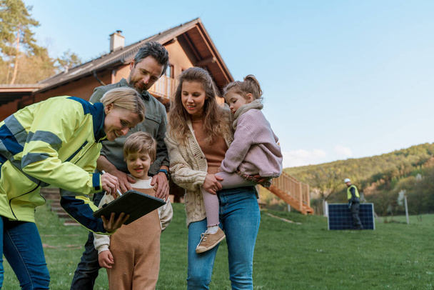 A woman engineer talking to young family about solar panel installation in front of their house. - Valokuva, kuva