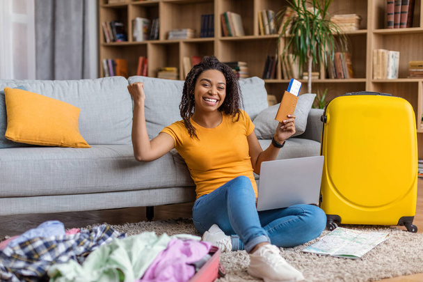 Overjoyed african american lady with passport and ticket gesturing YES, buying hot tour online on laptop from home. Online tickets booking, hotel reservation, summer vacation concept - Photo, image