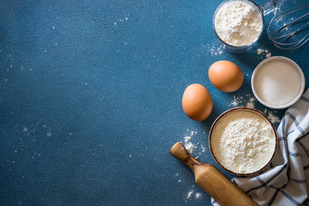 Baking background at blue stone table. Flour, sugar, eggs and utensil. Top view with copy space. - Photo, Image