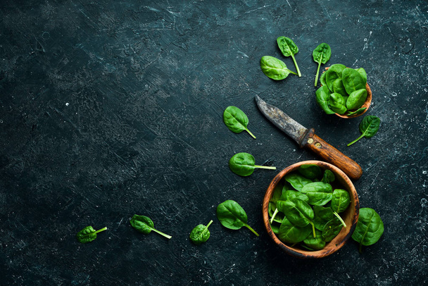 Fresh green spinach in a bowl. On a black stone background. Top view. - Photo, Image