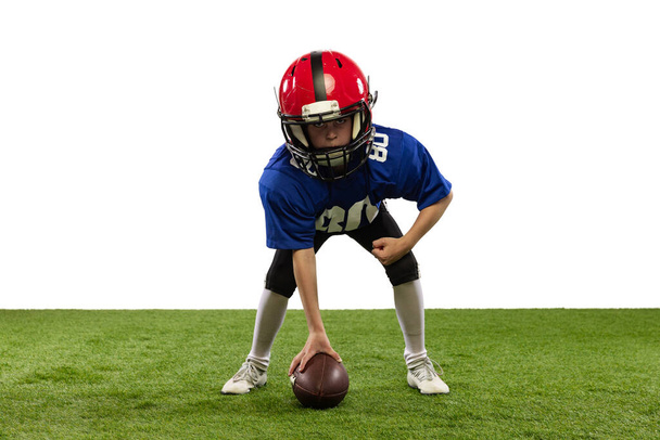 Starting position. Athletic kid, beginner american football player in sports uniform and helmet training isolated on white background. Concept of sport, challenges, action, achievements. - Fotó, kép