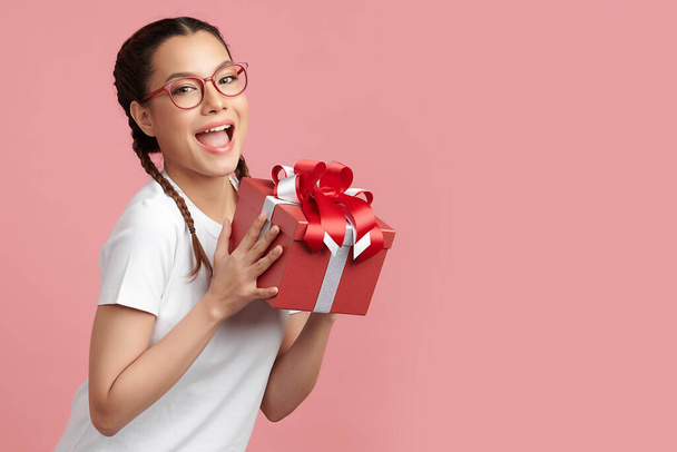Szczęśliwa ładna młoda kobieta trzyma pudełko na różowym tle, puste miejsce do kopiowania treści reklamowych. - Zdjęcie, obraz