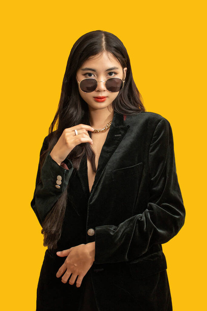 Moda koncepcja, Modna kobieta nosić czarny płaszcz i okulary do pozowania na żółtym tle. - Zdjęcie, obraz