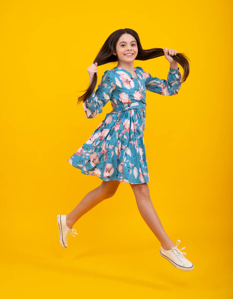 Full length cheerful teenager kid jump enjoy rejoice win isolated on yellow background. Small child girl in summer dress jumping. Fashion trendy kids look, child model in vogue fashionable style - Fotoğraf, Görsel